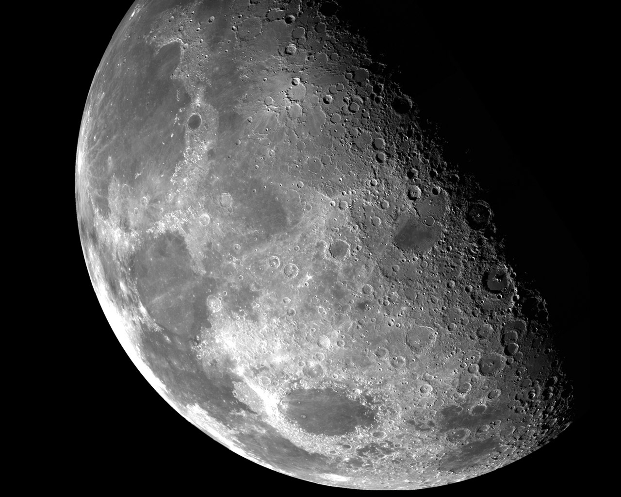 Detailed black and white photograph of the quarter Moon, showing highlands, maria, and topographic relief in the shadows along the terminator line